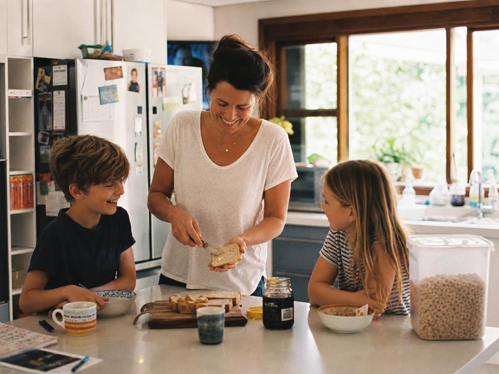 A parent making breakfast with two children in a sunlit kitchen